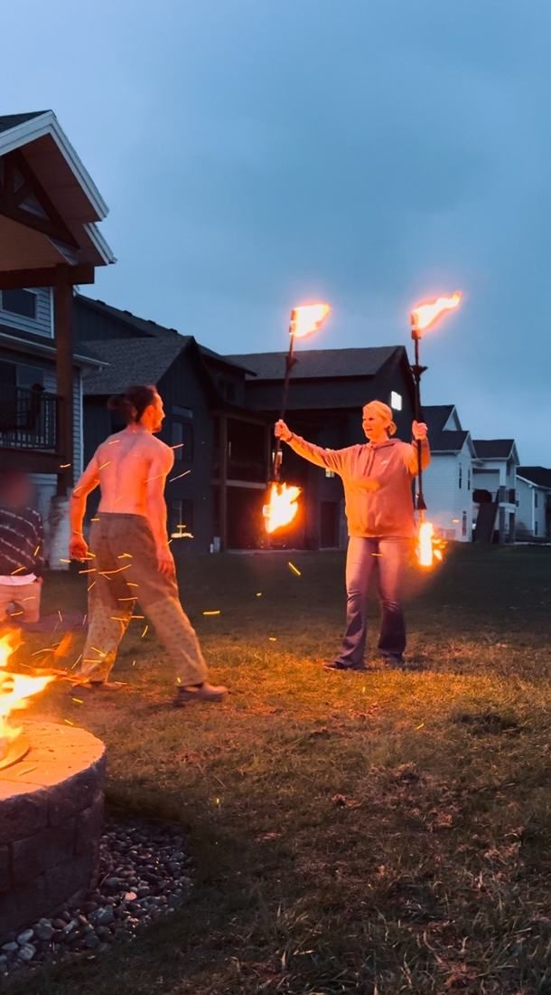 Tyler coaching a woman holding two lit fire staffs at dusk