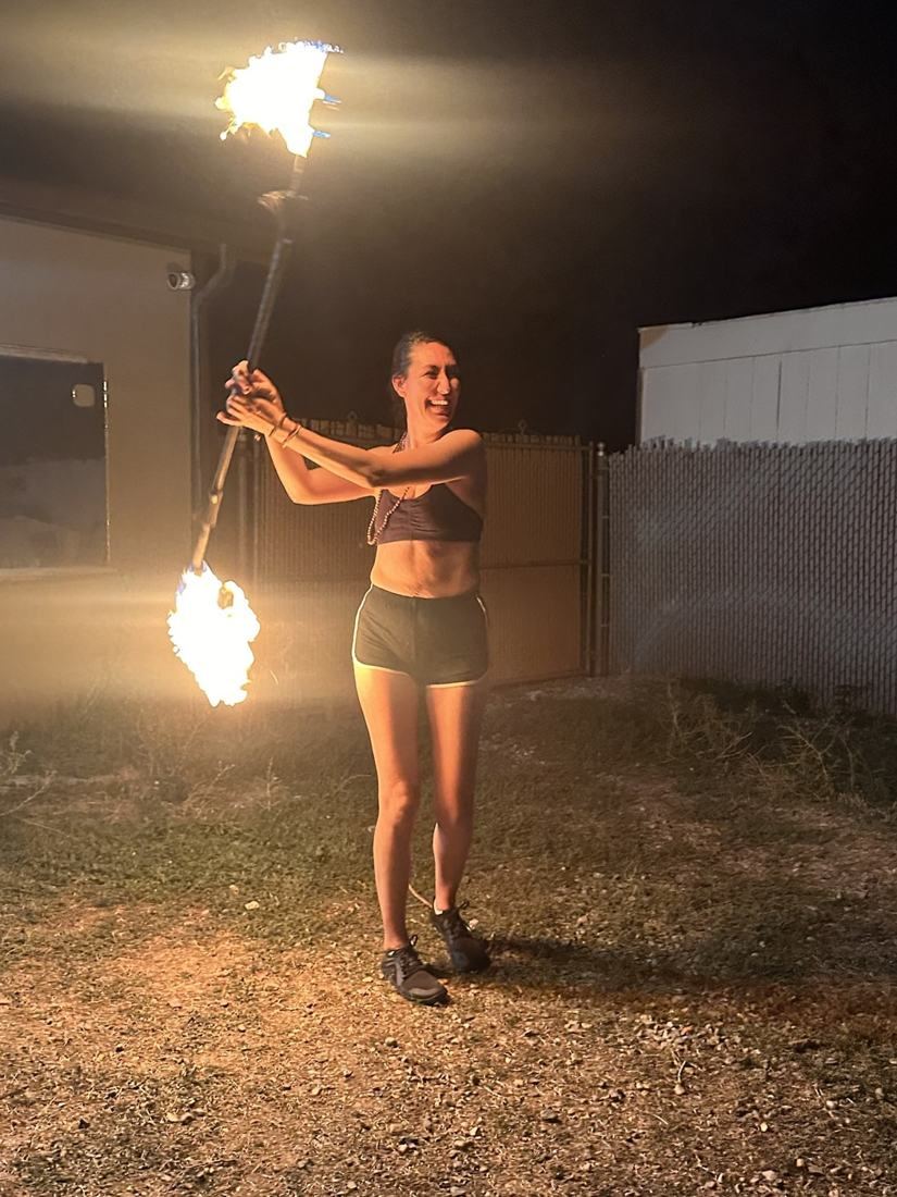 A woman laughing as she spins a lit fire staff overhead