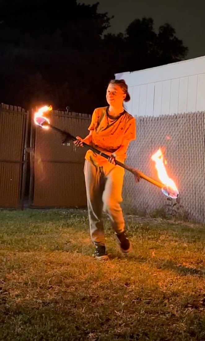 A first-time spinner smiling with a lit fire staff in a backyard