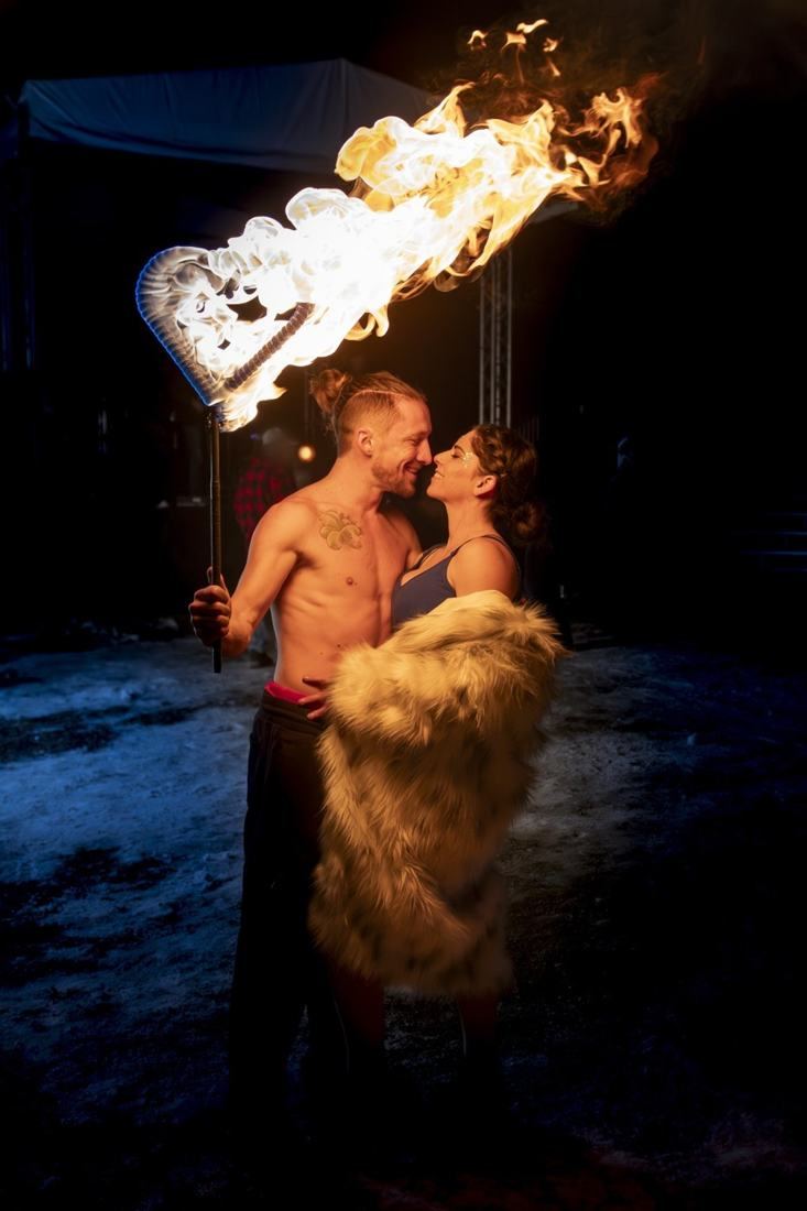 Tyler and a woman nose to nose beneath a blazing heart-shaped fire staff